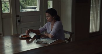 Movie still from “Antlers” (2021), directed by Scott Cooper – A woman sitting at a wooden table with a plate of food; Medium shot, High angle