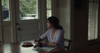 Movie still from “Antlers” (2021), directed by Scott Cooper – A woman sitting at a table with a cup of coffee; Medium shot, Over the shoulder angle