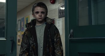 Movie still from “Antlers” (2021), directed by Scott Cooper – A young boy in a camo jacket standing in front of a door; Medium shot, Low angle