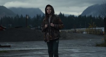 Movie still from “Antlers” (2021), directed by Scott Cooper – A young man in a hooded jacket standing in a parking lot; Wide shot, High angle