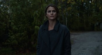 Movie still from “Antlers” (2021), directed by Scott Cooper – A woman standing in a wooded area with trees in the background; Close Up shot, Low angle