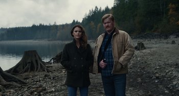Movie still from “Antlers” (2021), directed by Scott Cooper – A man and a woman standing next to a body of water; Wide shot, High angle