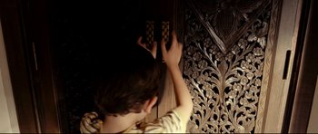Movie still from “The Impossible” (2012), directed by J.A. Bayona – A young boy playing a game of chess on a carved wooden wall; Close Up shot, Over the shoulder angle