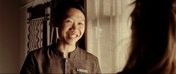 Movie still from “The Impossible” (2012), directed by J.A. Bayona – A young man smiling for the camera in front of a window; Close Up shot, Over the shoulder angle