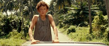 Movie still from “The Impossible” (2012), directed by J.A. Bayona – A young man standing on a road near trees; Medium shot, Low angle