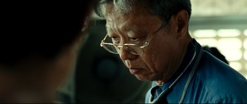 Movie still from “The Impossible” (2012), directed by J.A. Bayona – An older man wearing glasses looking down at something; Close Up shot, Over the shoulder angle