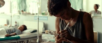 Movie still from “The Impossible” (2012), directed by J.A. Bayona – A man writing on a piece of paper; Close Up shot, Over the shoulder angle