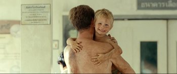 Movie still from “The Impossible” (2012), directed by J.A. Bayona – A shirtless man holding a young boy in his arms; Medium shot, Over the shoulder angle