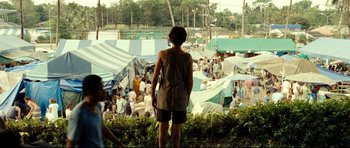 Movie still from “The Impossible” (2012), directed by J.A. Bayona – A man standing in front of a group of tents; Wide shot, Over the shoulder angle