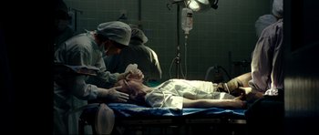 Movie still from “The Impossible” (2012), directed by J.A. Bayona – A man laying on a bed in a room with medical equipment; Medium shot, Low angle