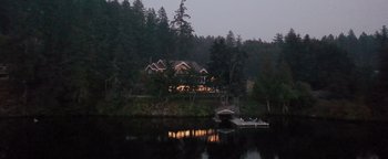Movie still from “Apex” (2021), directed by Edward Drake – A house on the water with a boat in the foreground; Extreme Wide shot, High angle