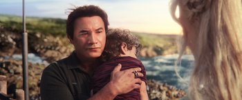Movie still from “Aquaman” (2018), directed by James Wan – A man holding a young child near a body of water; Close Up shot, Over the shoulder angle