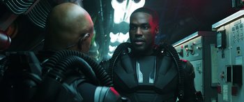 Movie still from “Aquaman” (2018), directed by James Wan – A man in a black suit is talking to another man in a black suit; Medium shot, Over the shoulder angle