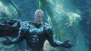 Movie still from “Aquaman” (2018), directed by James Wan – A man in a black suit standing in front of some plants; Medium shot, Over the shoulder angle