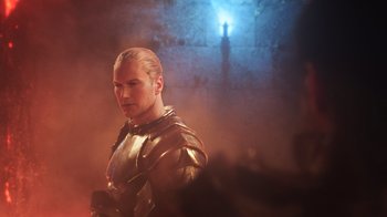Movie still from “Aquaman” (2018), directed by James Wan – A man wearing a golden armor standing in a dark room; Medium shot, Over the shoulder angle