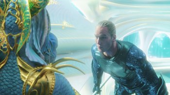 Movie still from “Aquaman” (2018), directed by James Wan – A man standing next to a dragon in a room; Medium shot, Over the shoulder angle