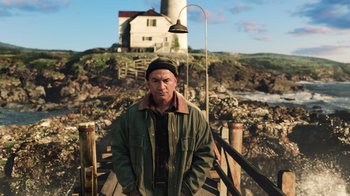 Movie still from “Aquaman” (2018), directed by James Wan – A man standing on top of a bridge near a light house; Medium shot, Low angle