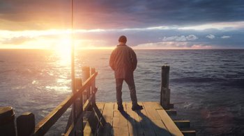 Movie still from “Aquaman” (2018), directed by James Wan – A man standing on a pier looking out at the ocean; Wide shot, Low angle