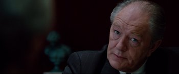 Movie still from “The Insider” (1999), directed by Michael Mann – An older man in a black suit looking at the camera; Close Up shot, Over the shoulder angle
