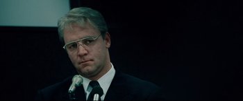Movie still from “The Insider” (1999), directed by Michael Mann – A man wearing a suit and tie while standing at a microphone; Close Up shot, Over the shoulder angle
