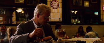 Movie still from “The Insider” (1999), directed by Michael Mann – A man sitting at a table eating a hot dog; Medium shot, Over the shoulder angle