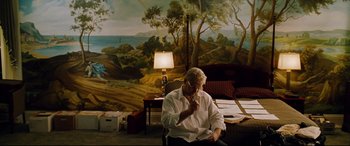 Movie still from “The Insider” (1999), directed by Michael Mann – An older man sitting in front of a painting; Wide shot, High angle