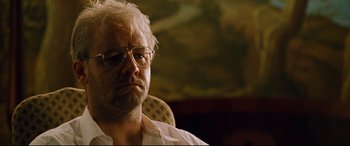 Movie still from “The Insider” (1999), directed by Michael Mann – A person sitting in a chair wearing glasses; Close Up shot, Low angle