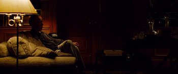 Movie still from “The Insider” (1999), directed by Michael Mann – A man sitting on a couch in a dark room; Medium shot, High angle