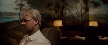 Movie still from “The Insider” (1999), directed by Michael Mann – A man sitting in a chair in front of a painting; Medium shot, Over the shoulder angle