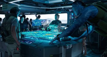 Movie still from “Avatar: The Way of Water” (2022), directed by James Cameron – A group of people are playing a video game on a computer screen; Wide shot, Over the shoulder angle