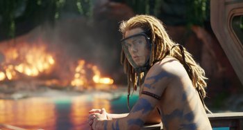 Movie still from “Avatar: The Way of Water” (2022), directed by James Cameron – A man with dreads is sitting in front of a fire; Medium shot, Over the shoulder angle