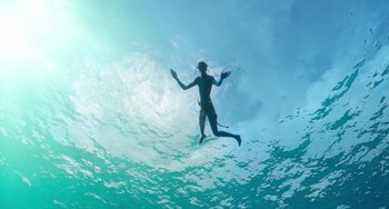 Movie still from “Avatar: The Way of Water” (2022), directed by James Cameron – A man swimming in a body of water; Wide shot, Low angle