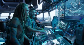 Movie still from “Avatar: The Way of Water” (2022), directed by James Cameron – A group of people sitting in a room with a computer; Medium shot, High angle