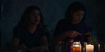 Movie still from “Awake” (2021), directed by Mark Raso – Two women sitting at a table in a dark room; Medium shot, Over the shoulder angle