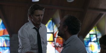 Movie still from “Awake” (2021), directed by Mark Raso – Two men are talking in front of a stained glass window; Medium shot, Low angle