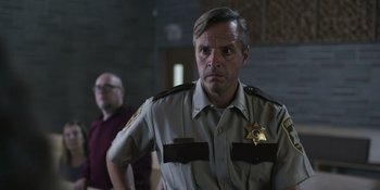 Movie still from “Awake” (2021), directed by Mark Raso – A man in a sheriff's uniform standing next to another man; Medium shot, Over the shoulder angle
