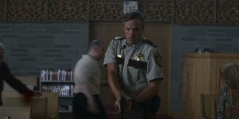 Movie still from “Awake” (2021), directed by Mark Raso – A man in a sheriff's uniform holding a gun; Medium shot, Low angle