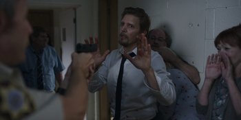Movie still from “Awake” (2021), directed by Mark Raso – A man in a white shirt and black neck tie is taking a picture of another man; Medium shot, Over the shoulder angle