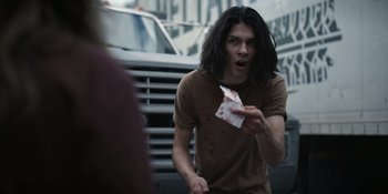 Movie still from “Awake” (2021), directed by Mark Raso – A man holding a piece of paper in front of a truck; Medium shot, Over the shoulder angle