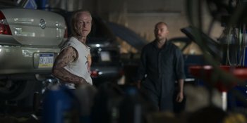 Movie still from “Awake” (2021), directed by Mark Raso – A man standing next to another man in a garage; Medium shot, Low angle