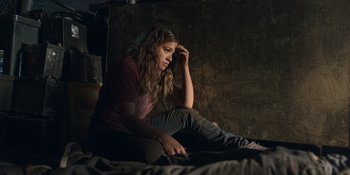 Movie still from “Awake” (2021), directed by Mark Raso – A woman sitting on the ground with her hand on her head; Medium shot, High angle