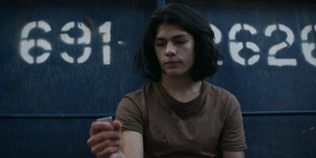 Movie still from “Awake” (2021), directed by Mark Raso – A young man sitting in front of a wall holding a cell phone; Close Up shot, Low angle