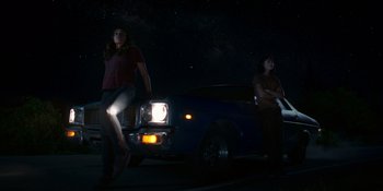 Movie still from “Awake” (2021), directed by Mark Raso – Two women standing in front of a car at night; Wide shot, Low angle