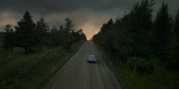 Movie still from “Awake” (2021), directed by Mark Raso – A car driving down a road near a forest; Extreme Wide shot, High angle