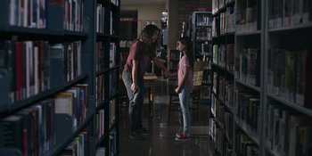 Movie still from “Awake” (2021), directed by Mark Raso – A woman and a girl are in a library; Wide shot, Over the shoulder angle