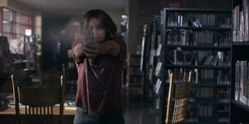 Movie still from “Awake” (2021), directed by Mark Raso – A woman holding a cell phone in a library; Medium shot, Low angle