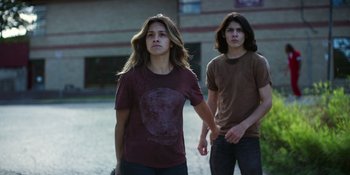 Movie still from “Awake” (2021), directed by Mark Raso – A woman and a man holding hands while standing in front of a building; Medium shot, Low angle