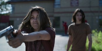 Movie still from “Awake” (2021), directed by Mark Raso – A woman with long brown hair is holding her arm out; Medium shot, Over the shoulder angle