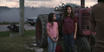 Movie still from “Awake” (2021), directed by Mark Raso – Two young girls standing in front of an old tractor; Medium shot, Over the shoulder angle