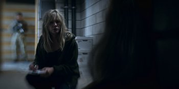 Movie still from “Awake” (2021), directed by Mark Raso – A woman sitting on a bench in a dark room; Medium shot, Over the shoulder angle